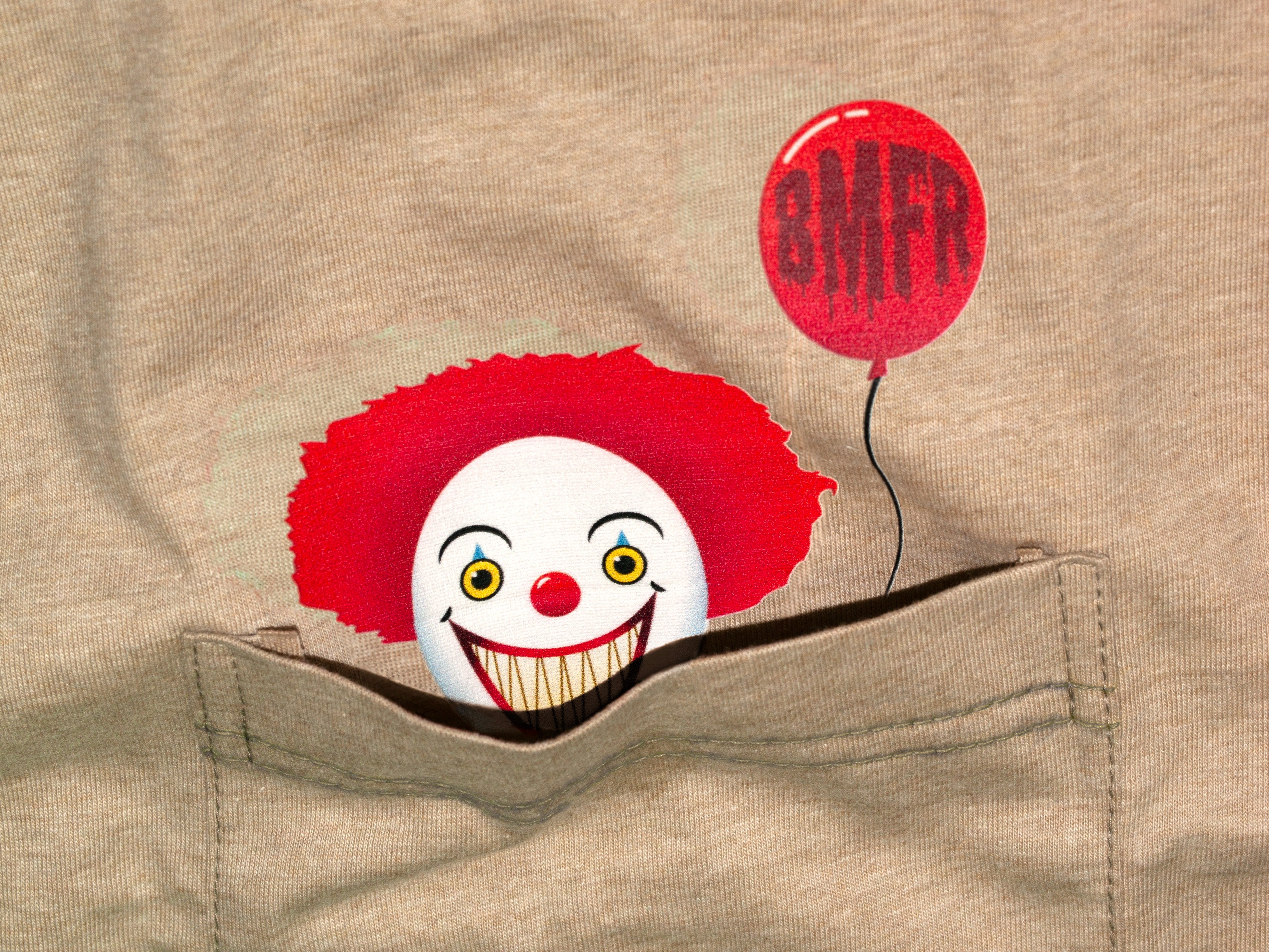 Clown face with red balloon popping out of a pocket on beige fabric